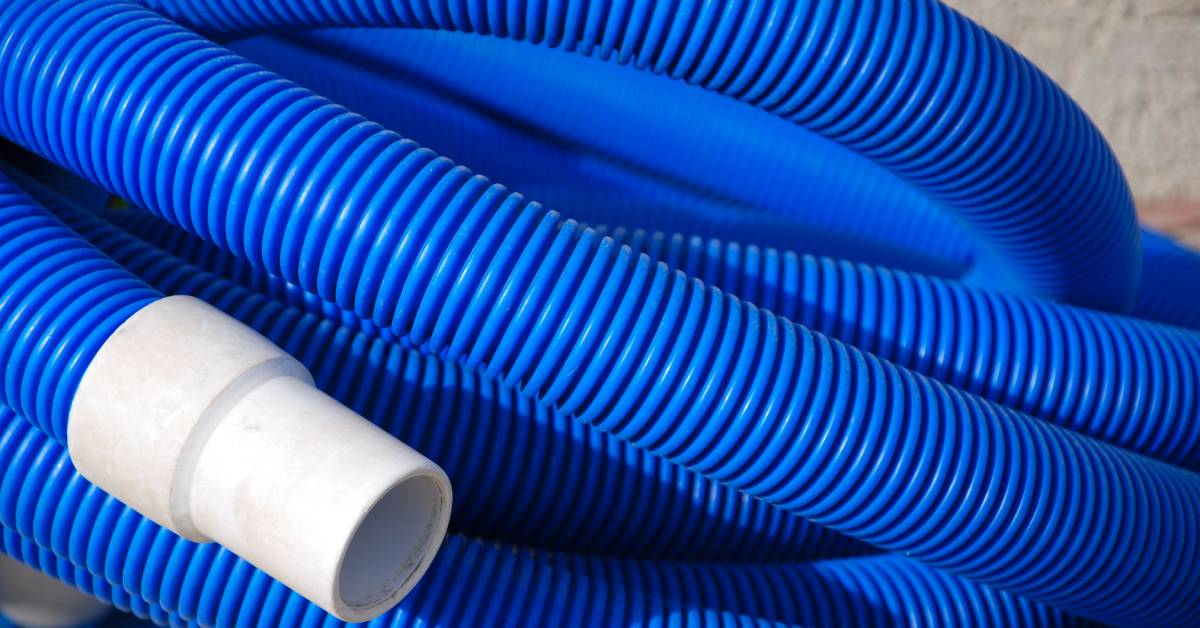 A close-up of a blue PVC hose loosely rolled up. One of its ends has a white connector piece attached.