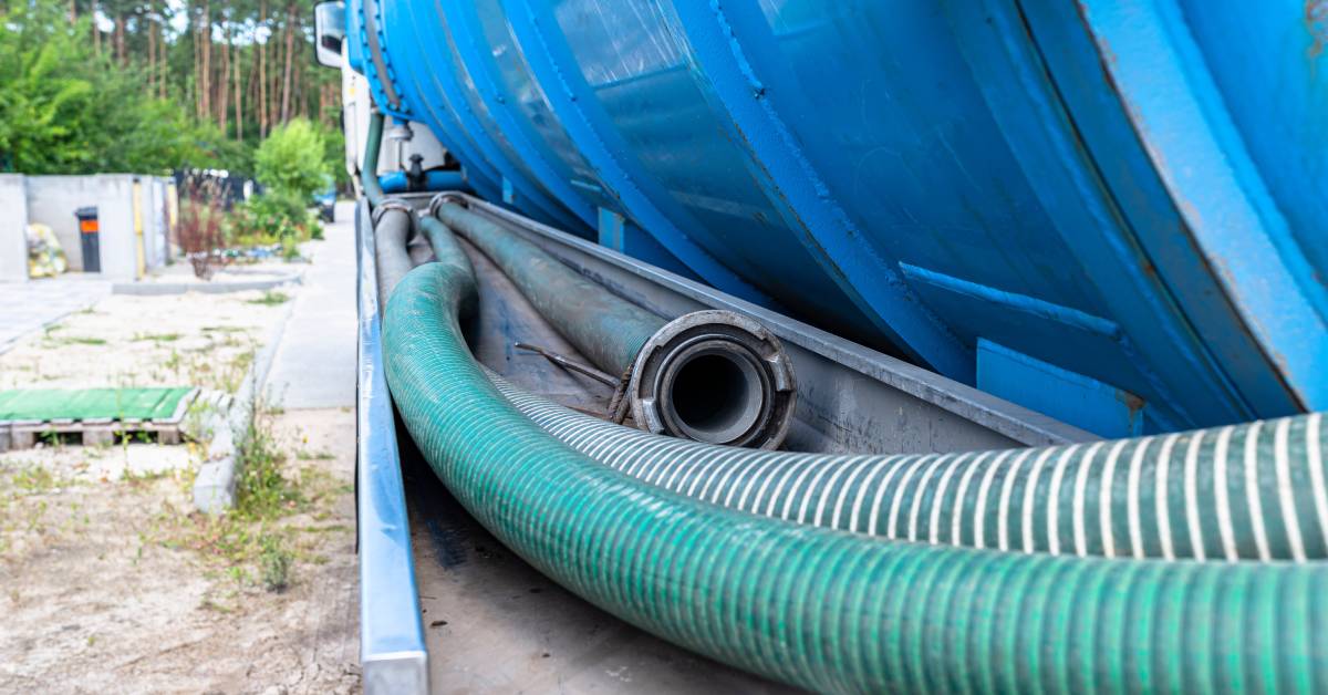 Three different teal-colored PVC suction hoses lined up in a row next to a blue septic tank at an outdoor site.