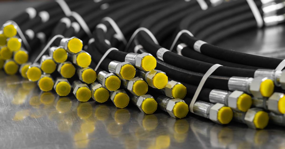 A collection of high-pressure hoses with black, rubber bodies, steel caps, and yellow stoppers on a metal surface.