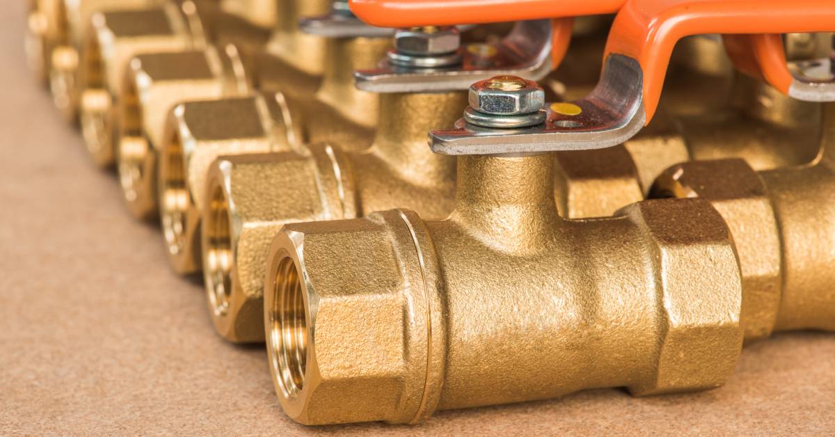 Numerous brass valves with orange handles lined up in rows on top of a brown, wooden or cork surface.